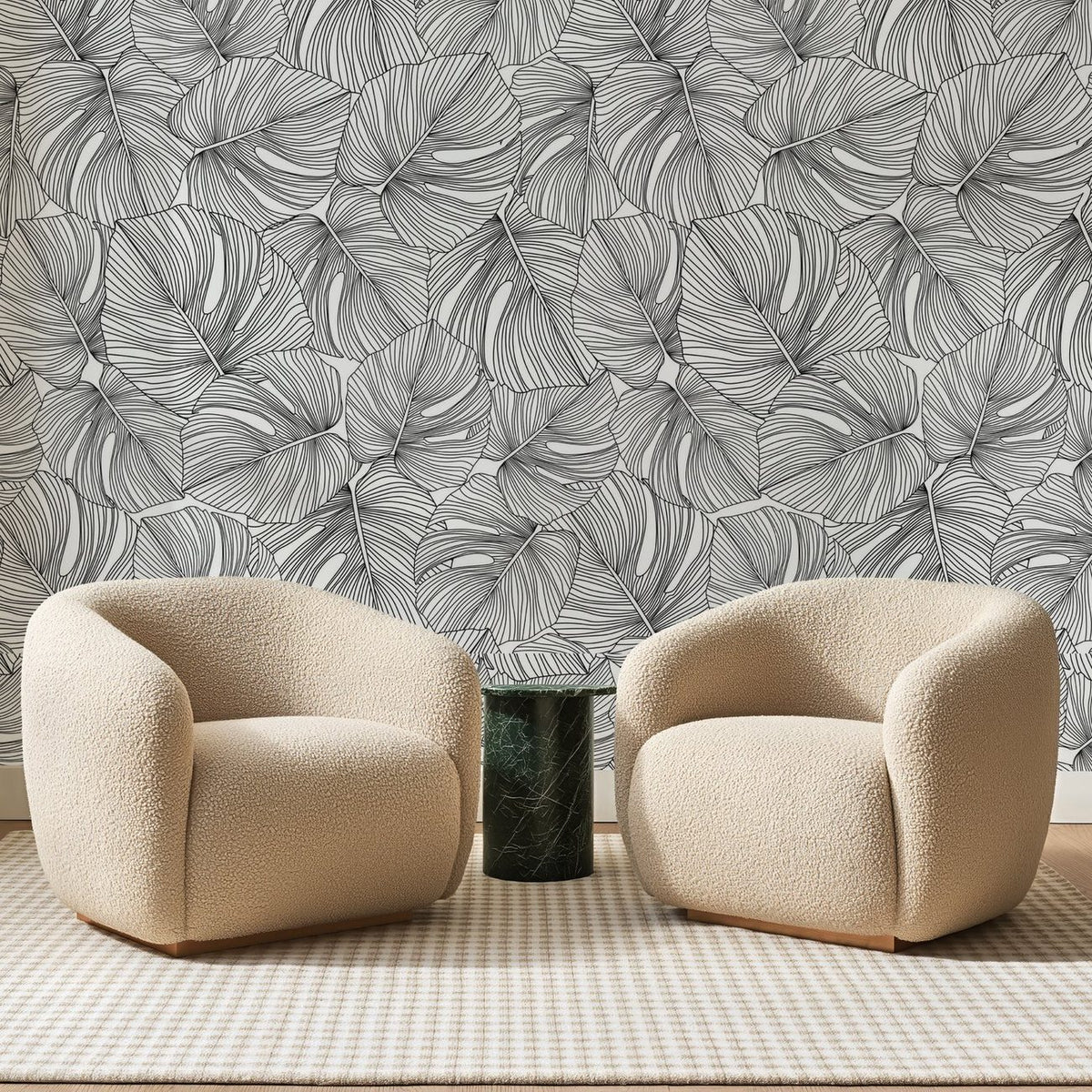Papier peint panoramique Monstera au Trait Noir, posé sur toute la paroi d'un salon, derrière deux fauteuils en bouclette crème et un guéridon en marbre vert