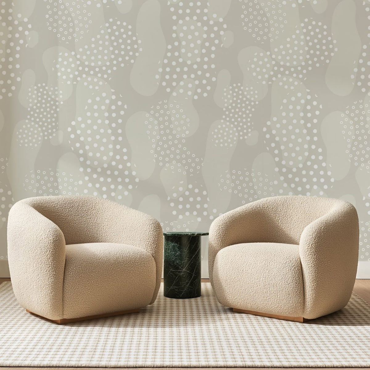Papier peint panoramique Galets à Pois Grège, posé sur toute la paroi d'un salon, derrière deux fauteuils en bouclette crème et un guéridon en marbre vert