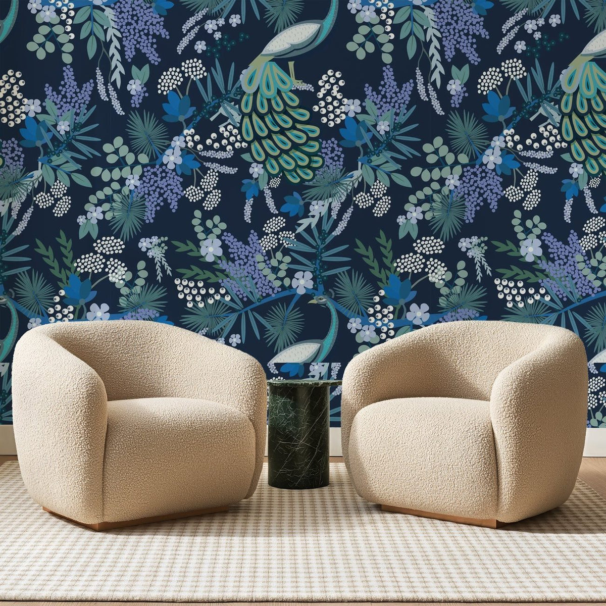 Papier peint panoramique Paon Fleuri Bleu Nuit, posé sur toute la paroi d'un salon, derrière deux fauteuils en bouclette crème et un guéridon en marbre vert