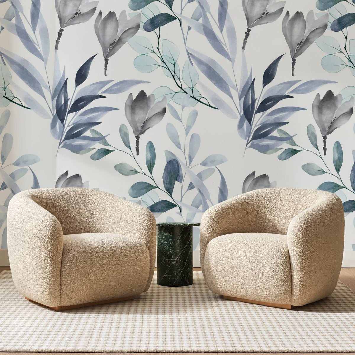 Papier peint panoramique Feuillage Aquarelle Bleu Ardoise, posé sur toute la paroi d'un salon, derrière deux fauteuils en bouclette crème et un guéridon en marbre vert