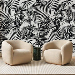 Papier peint panoramique Palmes à l'Encre Noire, posé sur toute la paroi d'un salon, derrière deux fauteuils en bouclette crème et un guéridon en marbre vert