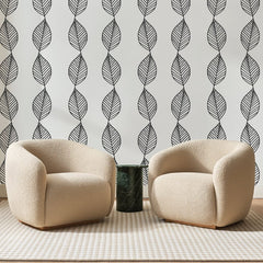 Papier peint panoramique Guirlandes de Feuilles Noires, posé sur toute la paroi d'un salon, derrière deux fauteuils en bouclette crème et un guéridon en marbre vert