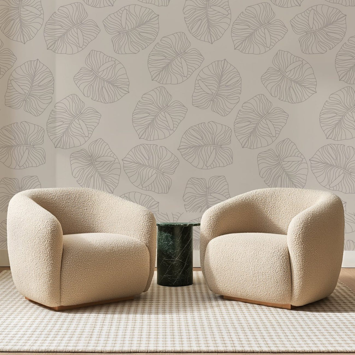 Papier peint panoramique Grandes Feuilles au Trait Greige, posé sur toute la paroi d'un salon, derrière deux fauteuils en bouclette crème et un guéridon en marbre vert