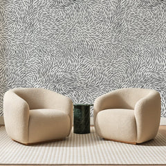 Papier peint panoramique Remous de Traits Noirs, posé sur toute la paroi d'un salon, derrière deux fauteuils en bouclette crème et un guéridon en marbre vert
