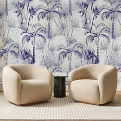 Papier peint panoramique Palmiers d'Encre Bleu Marine, posé sur toute la paroi d'un salon, derrière deux fauteuils en bouclette crème et un guéridon en marbre vert