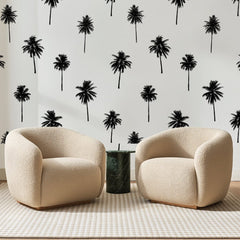 Papier peint panoramique Cocotiers Épars Noirs, posé sur toute la paroi d'un salon, derrière deux fauteuils en bouclette crème et un guéridon en marbre vert