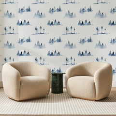 Papier peint panoramique Forêt Brumeuse Bleu Indigo, posé sur toute la paroi d'un salon, derrière deux fauteuils en bouclette crème et un guéridon en marbre vert