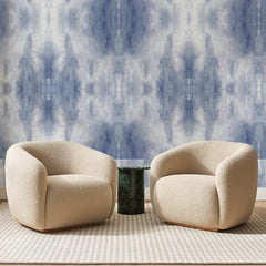 Papier peint panoramique Brume Délavée Bleu Ardoise, posé sur toute la paroi d'un salon, derrière deux fauteuils en bouclette crème et un guéridon en marbre vert