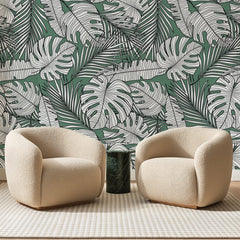 Papier peint panoramique Monstera au Trait sur Vert, posé sur toute la paroi d'un salon, derrière deux fauteuils en bouclette crème et un guéridon en marbre vert