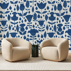 Papier peint panoramique Fleurs Folkloriques Bleu Indigo, posé sur toute la paroi d'un salon, derrière deux fauteuils en bouclette crème et un guéridon en marbre vert