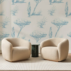 Papier peint panoramique Pins et Cyprès Bleus, posé sur toute la paroi d'un salon, derrière deux fauteuils en bouclette crème et un guéridon en marbre vert
