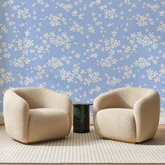 Papier peint panoramique Fleurettes Blanches Bleu Pervenche, posé sur toute la paroi d'un salon, derrière deux fauteuils en bouclette crème et un guéridon en marbre vert