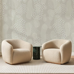Papier peint panoramique Galets à Pois Grège, posé sur toute la paroi d'un salon, derrière deux fauteuils en bouclette crème et un guéridon en marbre vert