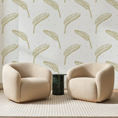 Papier peint panoramique Feuilles de Bananier Dorées, posé sur toute la paroi d'un salon, derrière deux fauteuils en bouclette crème et un guéridon en marbre vert