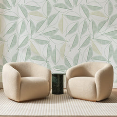 Papier peint panoramique Feuillage au Trait Vert Amande, posé sur toute la paroi d'un salon, derrière deux fauteuils en bouclette crème et un guéridon en marbre vert