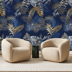 Papier peint panoramique Feuillage Tropical Or sur Bleu Nuit, posé sur toute la paroi d'un salon, derrière deux fauteuils en bouclette crème et un guéridon en marbre vert