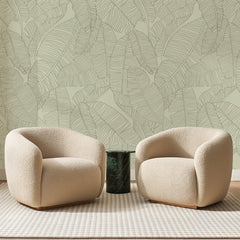 Papier peint panoramique Bananiers au Trait Vert Pâle, posé sur toute la paroi d'un salon, derrière deux fauteuils en bouclette crème et un guéridon en marbre vert