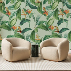 Papier peint panoramique Perroquets sur Vert Amande, posé sur toute la paroi d'un salon, derrière deux fauteuils en bouclette crème et un guéridon en marbre vert