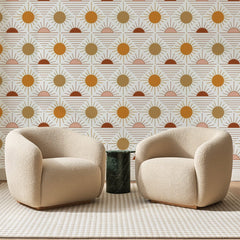 Papier peint panoramique Soleils Levants Ocre et Rose, posé sur toute la paroi d'un salon, derrière deux fauteuils en bouclette crème et un guéridon en marbre vert
