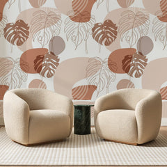 Papier peint panoramique Monstera au Trait Terracotta, posé sur toute la paroi d'un salon, derrière deux fauteuils en bouclette crème et un guéridon en marbre vert