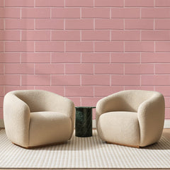 Papier peint panoramique Briques Roses Poudrées, posé sur toute la paroi d'un salon, derrière deux fauteuils en bouclette crème et un guéridon en marbre vert
