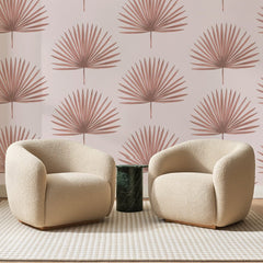 Papier peint panoramique Palmes Éventail Rose Poudré, posé sur toute la paroi d'un salon, derrière deux fauteuils en bouclette crème et un guéridon en marbre vert