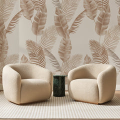 Papier peint panoramique Palmes Terracotta sur Sable, posé sur toute la paroi d'un salon, derrière deux fauteuils en bouclette crème et un guéridon en marbre vert