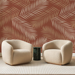 Papier peint panoramique Palmes Sable sur Terracotta, posé sur toute la paroi d'un salon, derrière deux fauteuils en bouclette crème et un guéridon en marbre vert