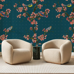 Papier peint panoramique Cerisiers et Mésanges Bleu Paon, posé sur toute la paroi d'un salon, derrière deux fauteuils en bouclette crème et un guéridon en marbre vert