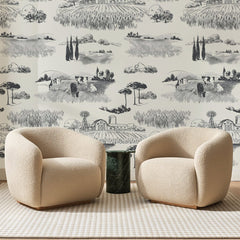 Papier peint panoramique Campagne à l'Encre Noire, posé sur toute la paroi d'un salon, derrière deux fauteuils en bouclette crème et un guéridon en marbre vert.