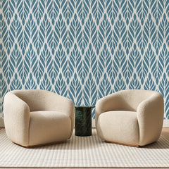 Papier peint panoramique Feuilles Tressées Bleu Acier, posé sur toute la paroi d'un salon, derrière deux fauteuils en bouclette crème et un guéridon en marbre vert