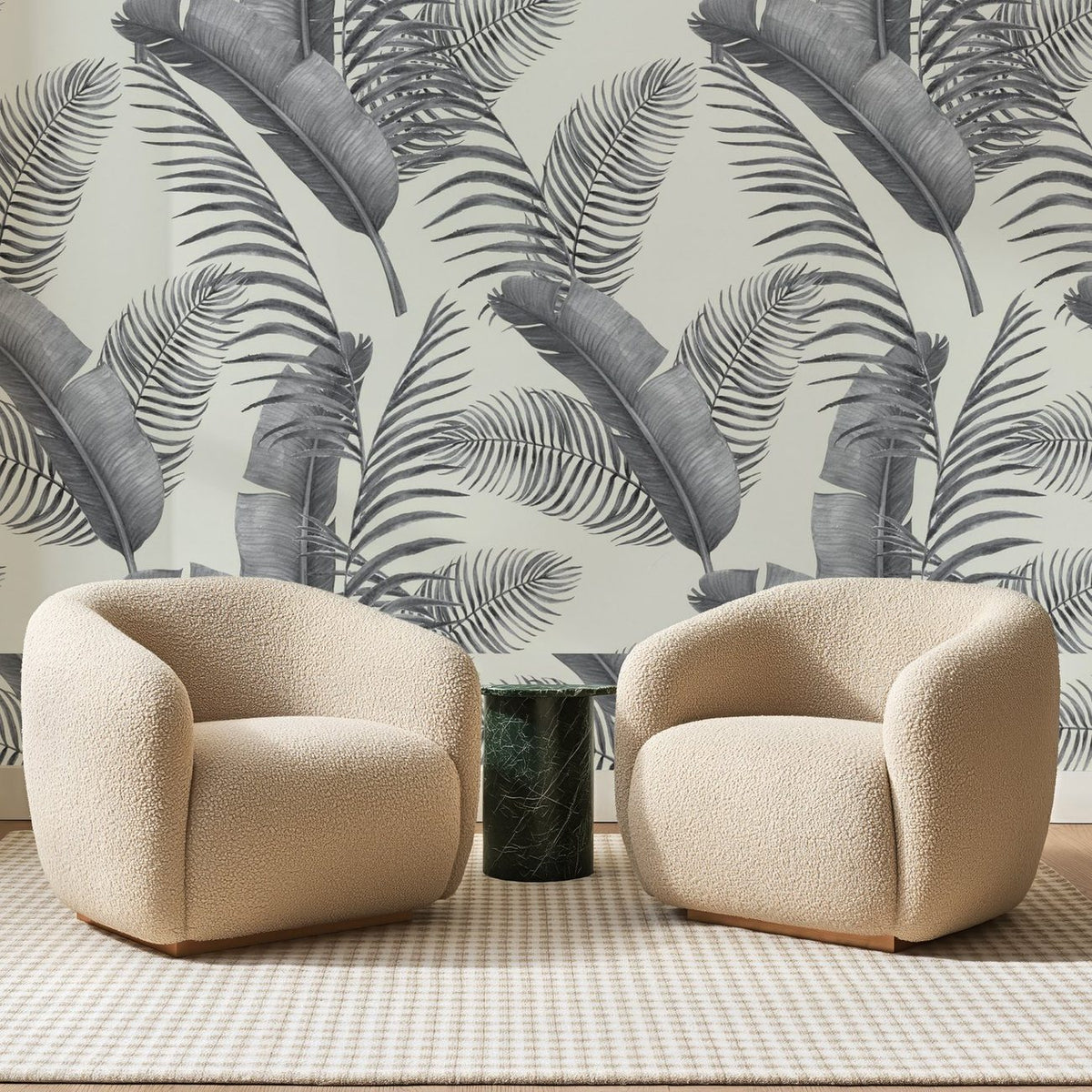 Papier peint panoramique Palmes Grises sur Ivoire, posé sur toute la paroi d'un salon, derrière deux fauteuils en bouclette crème et un guéridon en marbre vert.