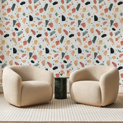 Papier peint panoramique Granito Peint Corail Et Sauge, posé sur toute la paroi d'un salon, derrière deux fauteuils en bouclette crème et un guéridon en marbre vert