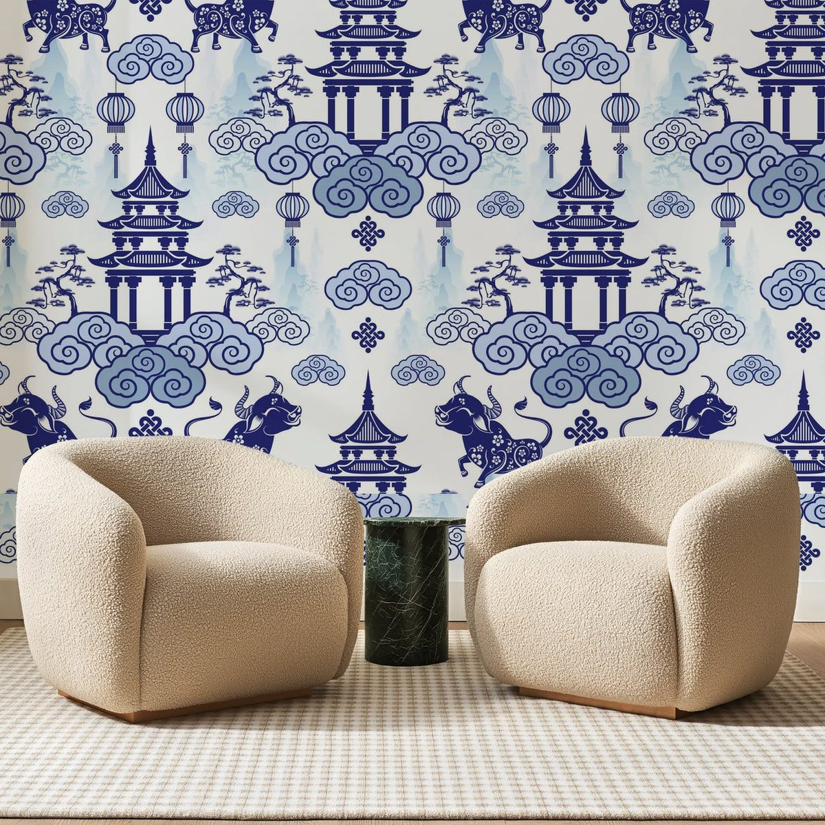 Papier peint panoramique Pagodes et Buffles Bleu Porcelaine, posé sur toute la paroi d'un salon, derrière deux fauteuils en bouclette crème et un guéridon en marbre vert
