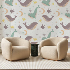 Papier peint panoramique Baleines Étoilées Mauve Pâle, posé sur toute la paroi d'un salon, derrière deux fauteuils en bouclette crème et un guéridon en marbre vert
