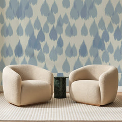 Papier peint panoramique Gouttes Ikat Bleu Ardoise, posé sur toute la paroi d'un salon, derrière deux fauteuils en bouclette crème et un guéridon en marbre vert