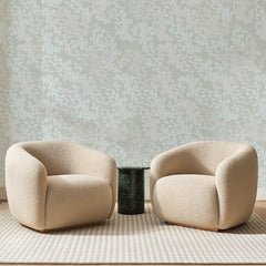 Papier peint panoramique Rameaux Givrés Vert Amande, posé sur toute la paroi d'un salon, derrière deux fauteuils en bouclette crème et un guéridon en marbre vert