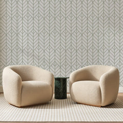 Papier peint panoramique Feuilles Art Déco Taupe, posé sur toute la paroi d'un salon, derrière deux fauteuils en bouclette crème et un guéridon en marbre vert
