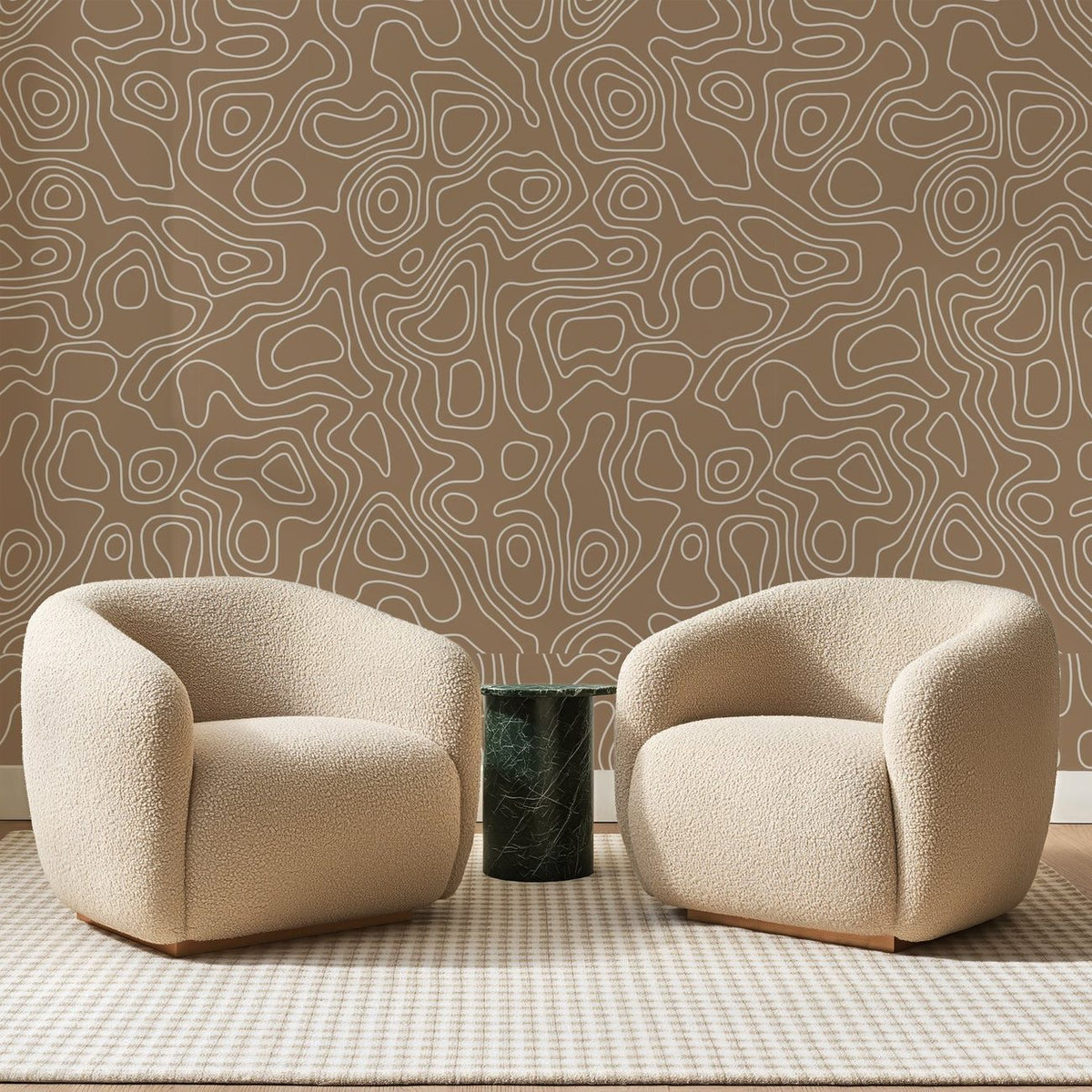 Papier peint panoramique Courbes de Niveau Caramel, posé sur toute la paroi d'un salon, derrière deux fauteuils en bouclette crème et un guéridon en marbre vert.