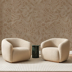 Papier peint panoramique Courbes de Niveau Caramel, posé sur toute la paroi d'un salon, derrière deux fauteuils en bouclette crème et un guéridon en marbre vert.