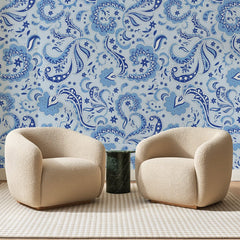Papier peint panoramique Cachemire Bandana Bleu, posé sur toute la paroi d'un salon, derrière deux fauteuils en bouclette crème et un guéridon en marbre vert