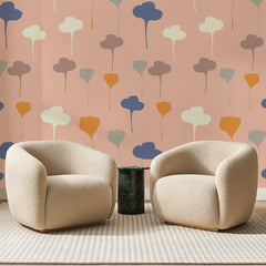 Papier peint panoramique Corolles Pastel sur Rose Pêche, posé sur toute la paroi d'un salon, derrière deux fauteuils en bouclette crème et un guéridon en marbre vert.