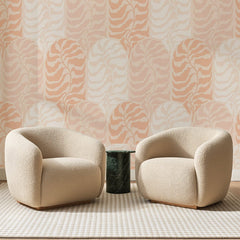 Papier peint panoramique Dômes Ondulés Rose Pêche, posé sur toute la paroi d'un salon, derrière deux fauteuils en bouclette crème et un guéridon en marbre vert
