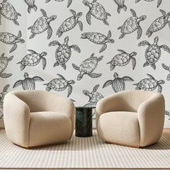 Papier peint panoramique Tortues Marines Encre Noire, posé sur toute la paroi d'un salon, derrière deux fauteuils en bouclette crème et un guéridon en marbre vert