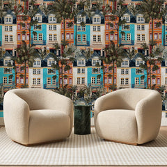 Papier peint panoramique Façades Méditerranéennes Terracotta, posé sur toute la paroi d'un salon, derrière deux fauteuils en bouclette crème et un guéridon en marbre vert