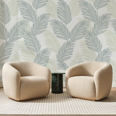 Papier peint panoramique Palmes Bleu Ardoise et Sable, posé sur toute la paroi d'un salon, derrière deux fauteuils en bouclette crème et un guéridon en marbre vert