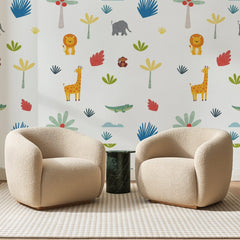 Papier peint panoramique Animaux et Arbres Multicolores, posé sur toute la paroi d'un salon, derrière deux fauteuils en bouclette crème et un guéridon en marbre vert
