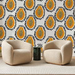 Papier peint panoramique Papayes Orange sur Blanc, posé sur toute la paroi d'un salon, derrière deux fauteuils en bouclette crème et un guéridon en marbre vert