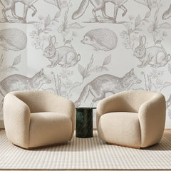 Papier peint panoramique Animaux de la Forêt Taupe, posé sur toute la paroi d'un salon, derrière deux fauteuils en bouclette crème et un guéridon en marbre vert