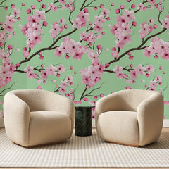 Papier peint panoramique Cerisier En Fleurs Vert Amande, posé sur toute la paroi d'un salon, derrière deux fauteuils en bouclette crème et un guéridon en marbre vert